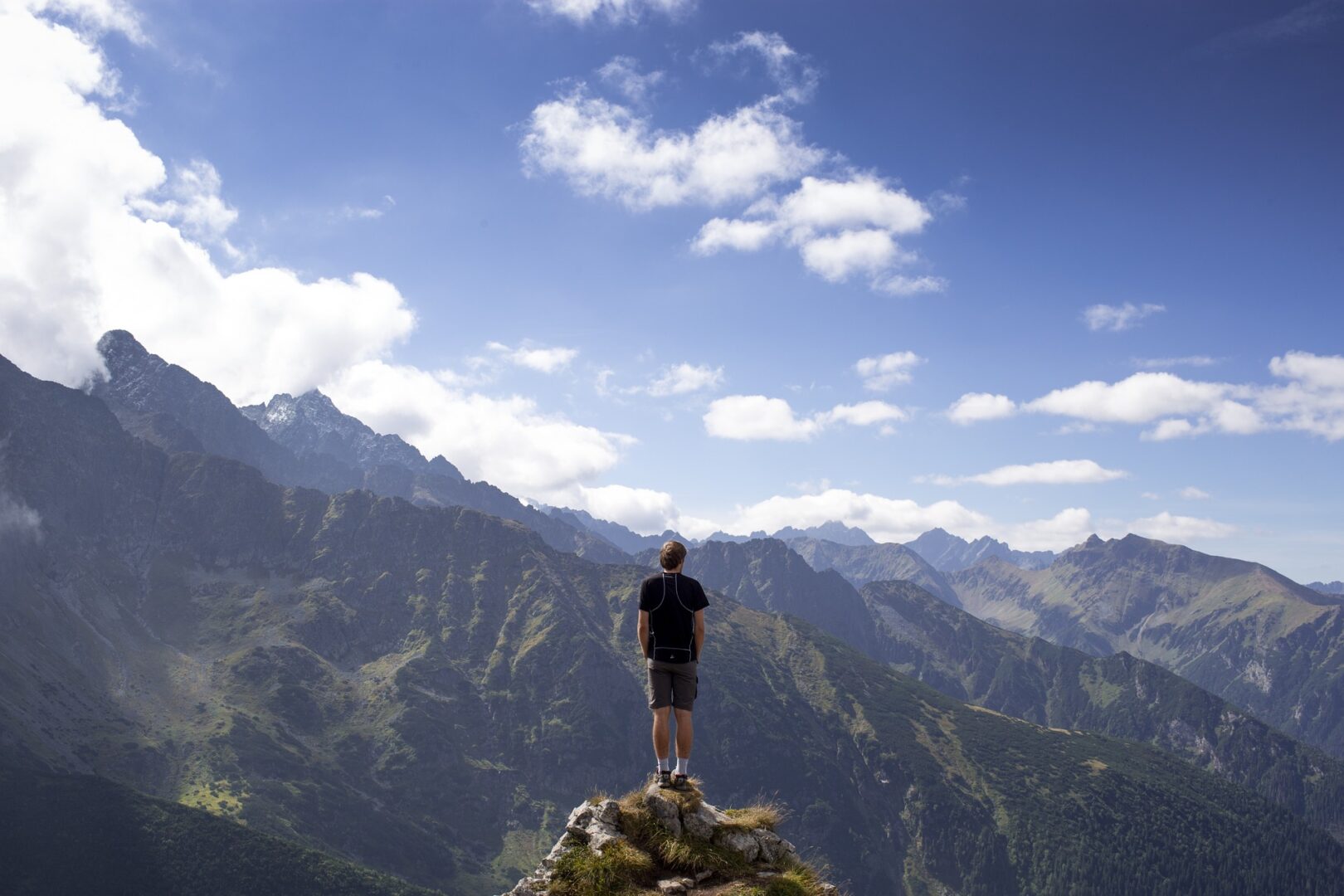 Man standing atop a mountain looking at the view and the sky